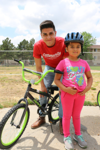 A young man wearing a red shirt with a child wearing a helmet and close to her bike